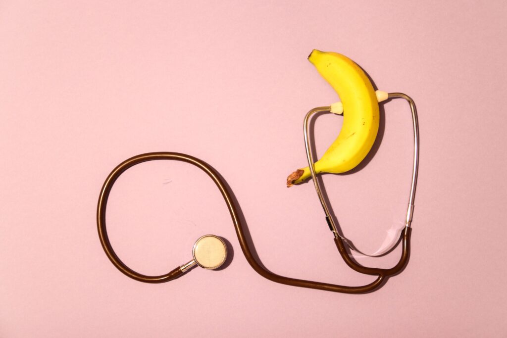علاج تاخير القذف A banana wrapped in a stethoscope on a pink surface, symbolizing health check themes.