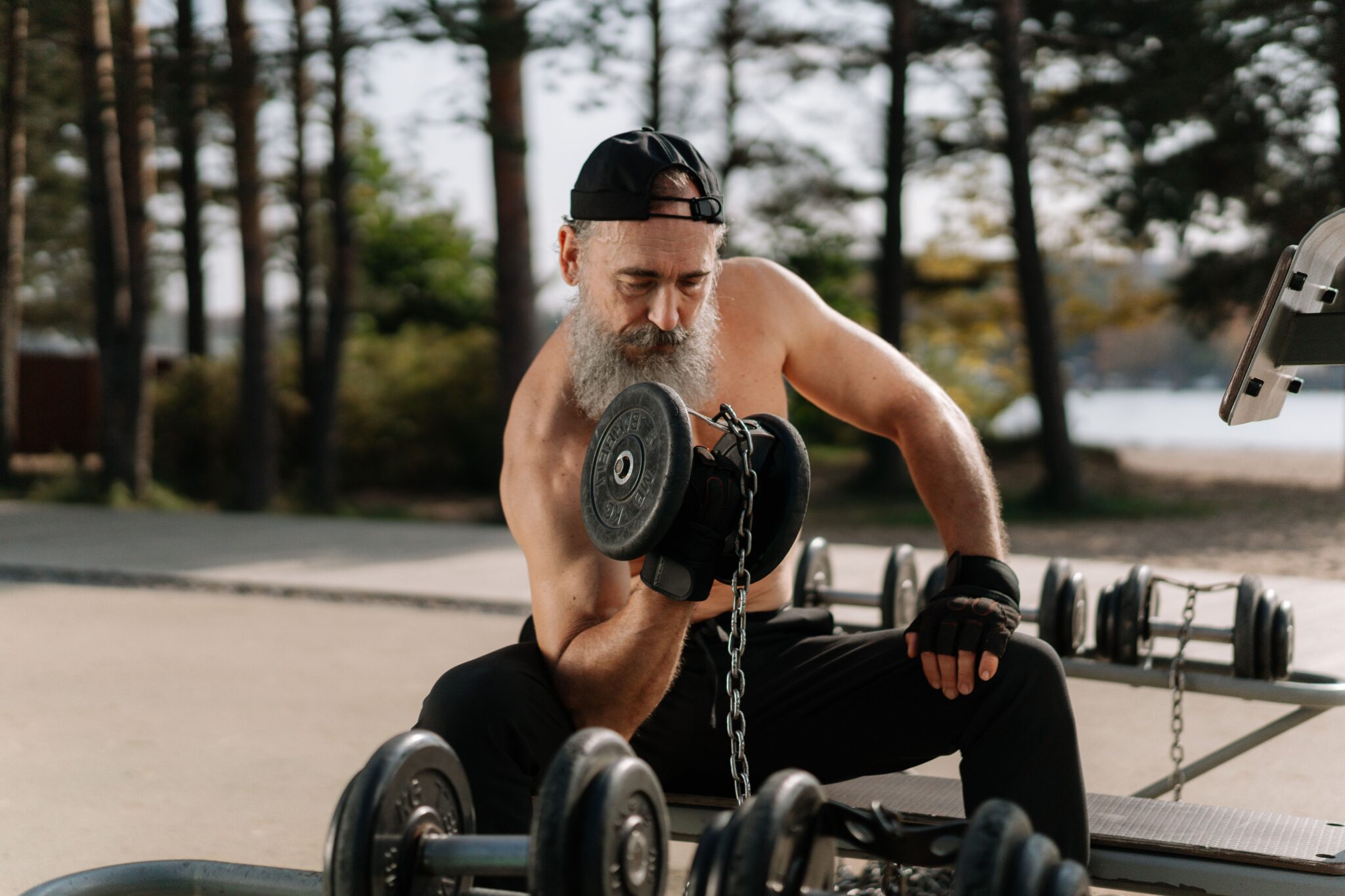 Elderly man lifting dumbbells in an outdoor gym setting, promoting healthy lifestyle.