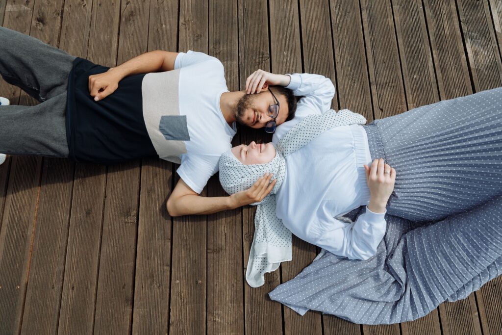 Couple relaxing on a wooden dock, sharing an affectionate moment in a serene outdoor setting.